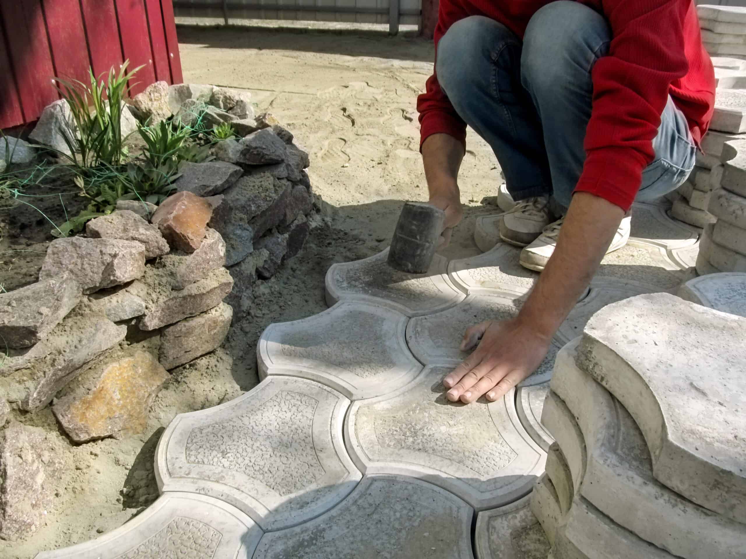 A worker holds a rubber hammer in his hand and does the work of laying paving slabs. The concept of laying paving tiles on the patio, courtyard, garden and other sites